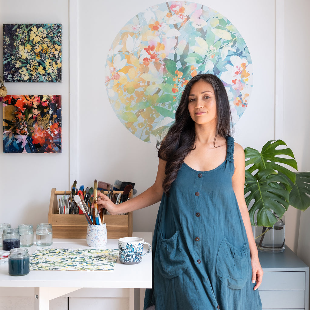 Artist Ingrid Sanchez in her studio with In Full Bloom teal wall sticker behind her, original watercolor art