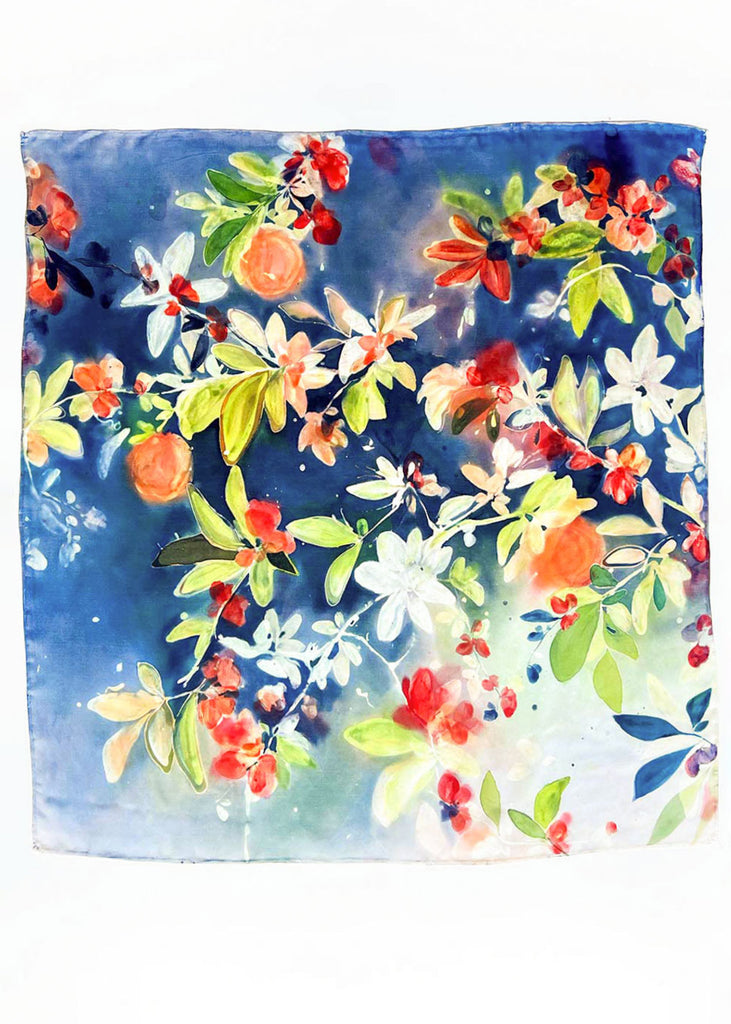 ‘Citrus Passion Grove’ is an original, one-of-a-kind piece painted by hand using vibrant dyes on 100% silk. This design is a celebration of nature’s vibrancy, featuring glowing citrus tones of orange, red, and soft white blossoms against a rich blue backdrop. Hints of lush green leaves weave through the composition, creating a lively and fresh atmosphere. Ingrid Sanchez, 2025, CreativeIngrid.